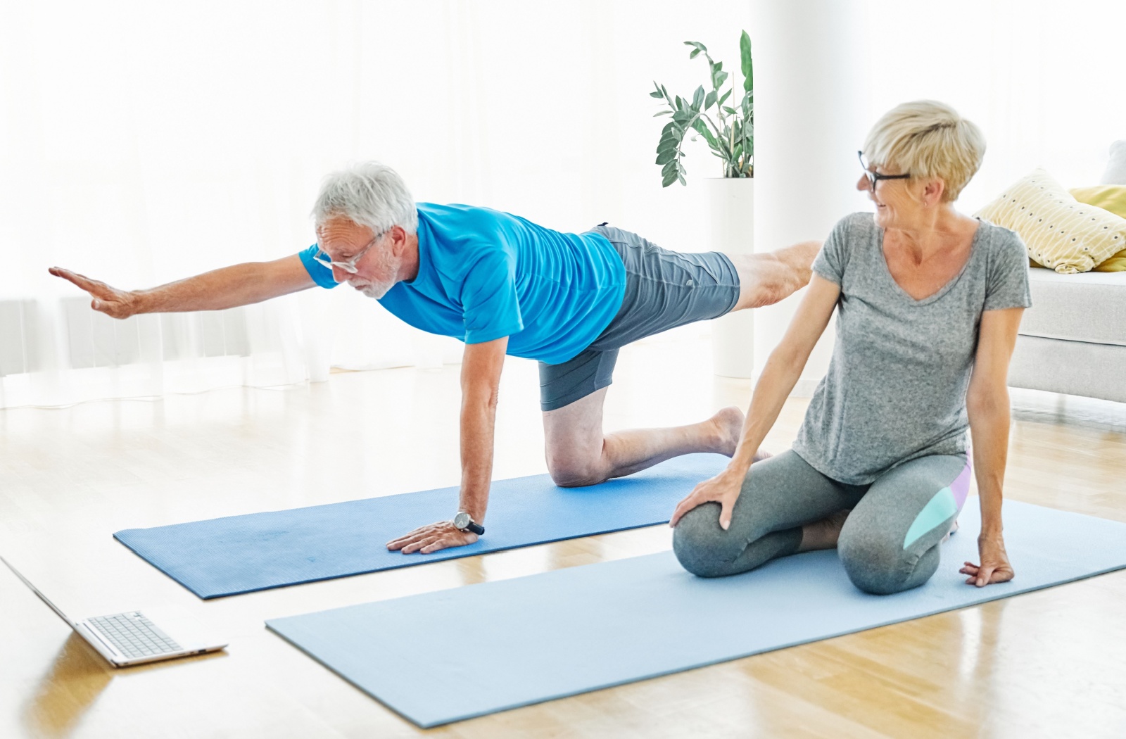 A senior couple try gentle yoga together using an online tutorial on a laptop