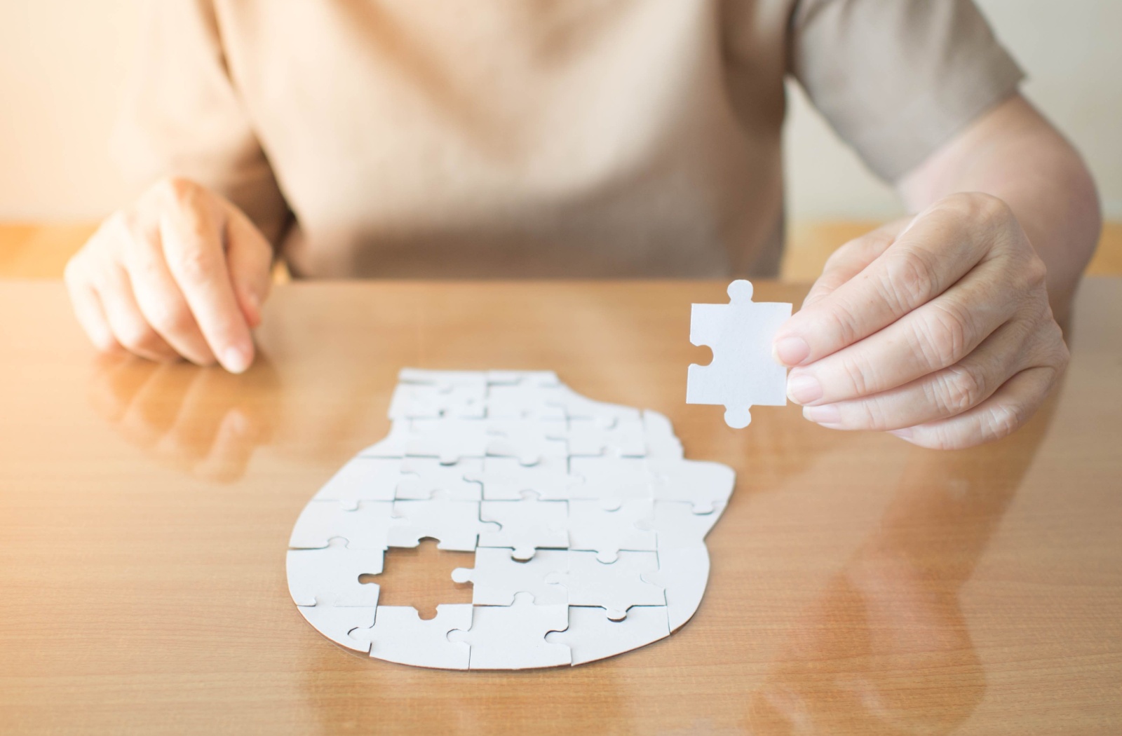 A person holds up a puzzle piece that has been removed from a jigsaw puzzle of a human head.