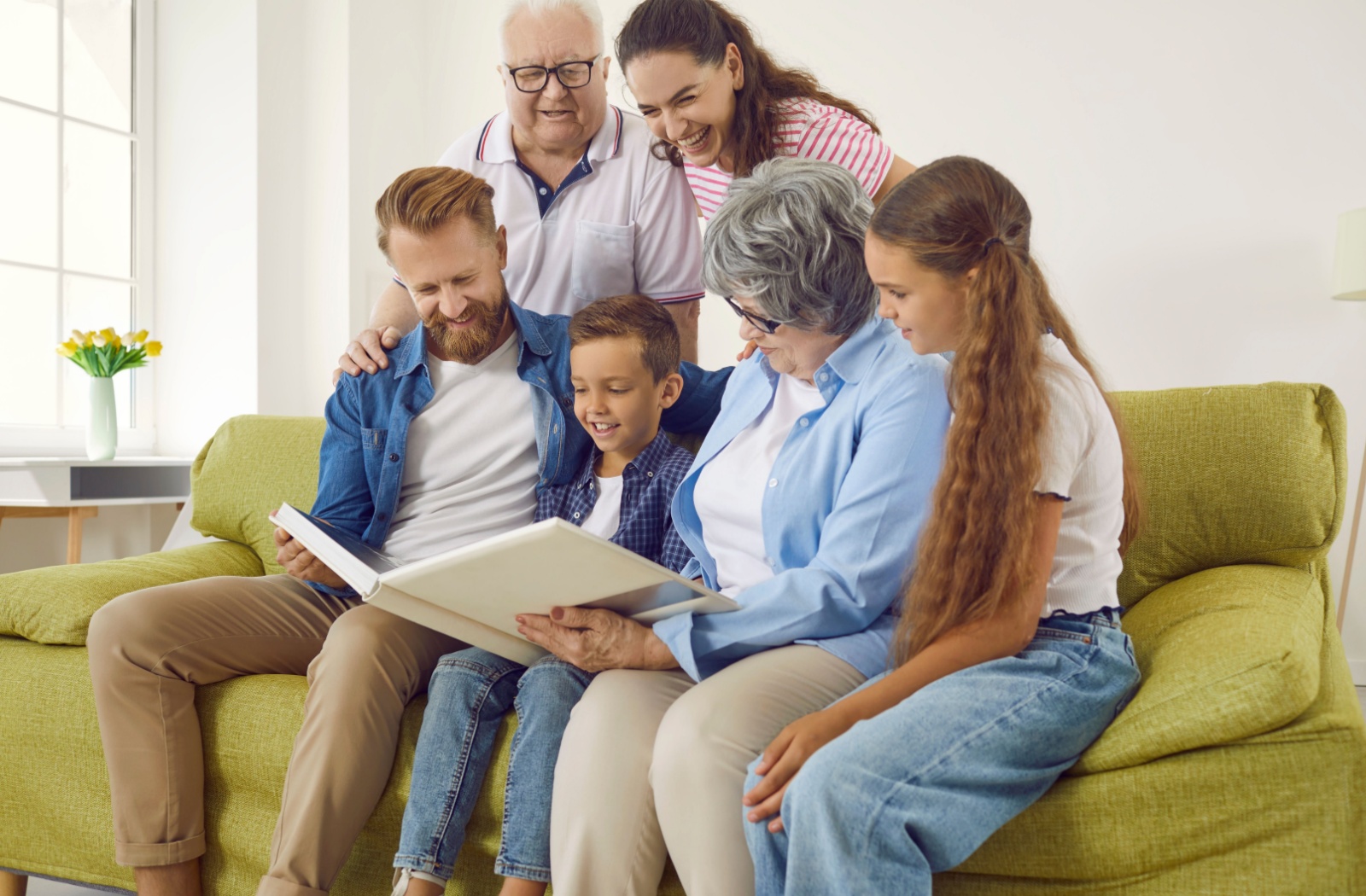 Several generations of family members sitting on a couch looking through a photo album with their grandmother with Alzheimer's.