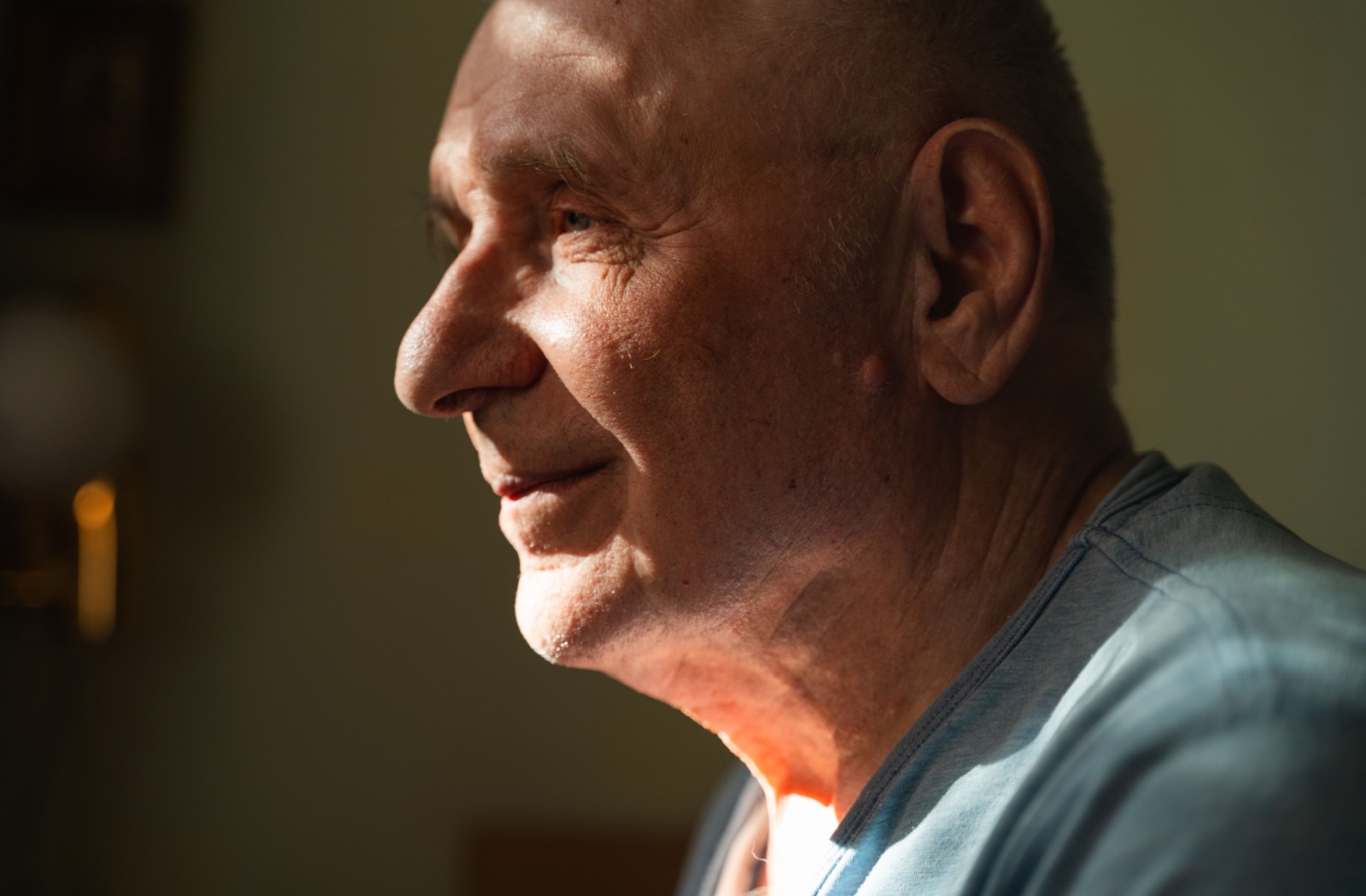 A senior with memory loss sits in bed as light sneaks through the blinds.