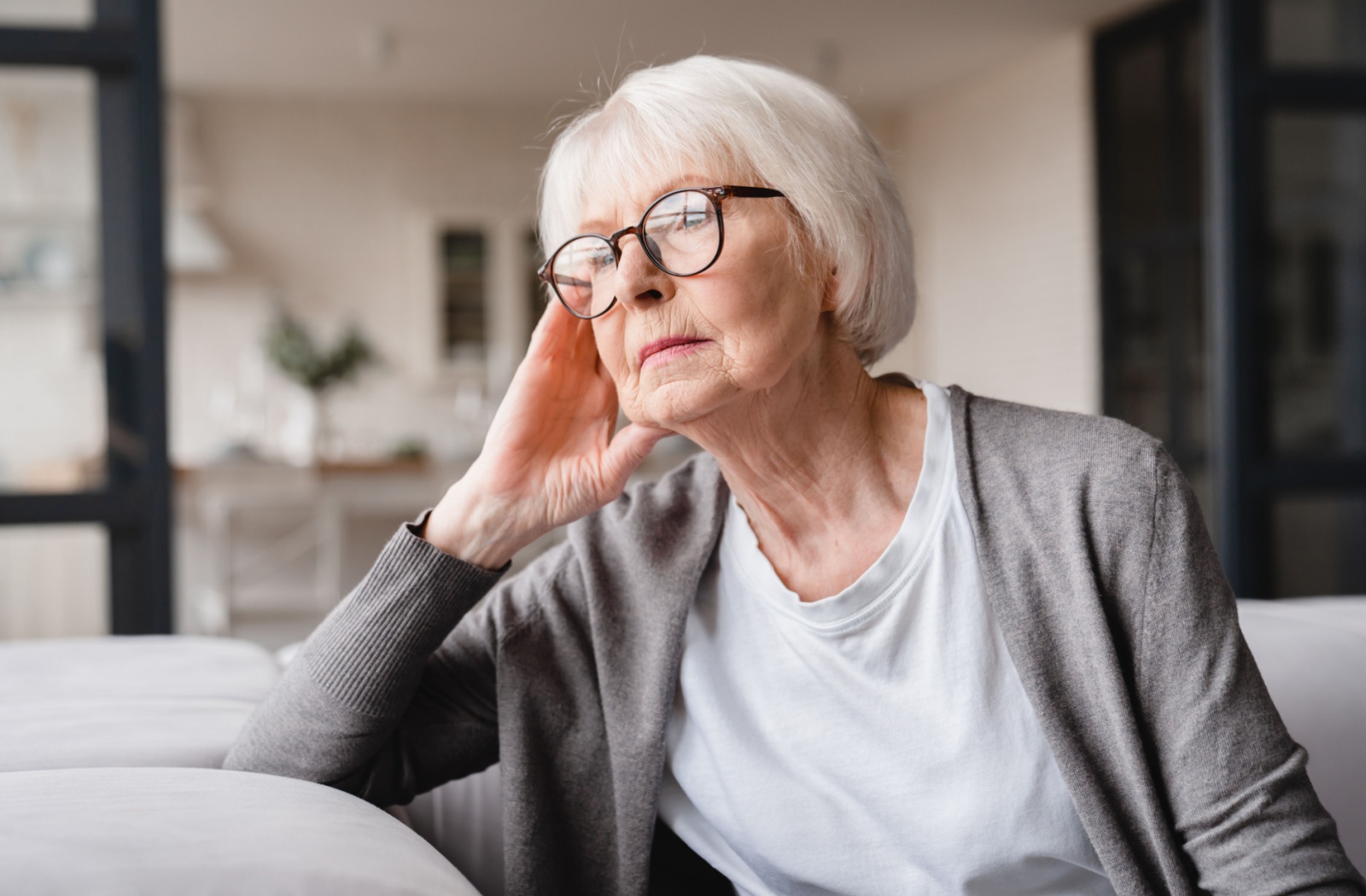 An older adult with memory loss sitting on a couch and staring out the window.