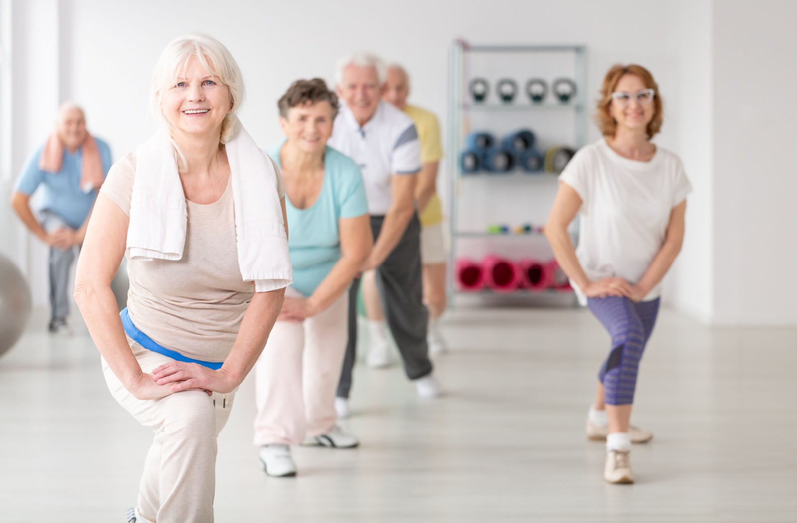 A group of older adults with dementia in memory care lightly stretching during an exercise class.