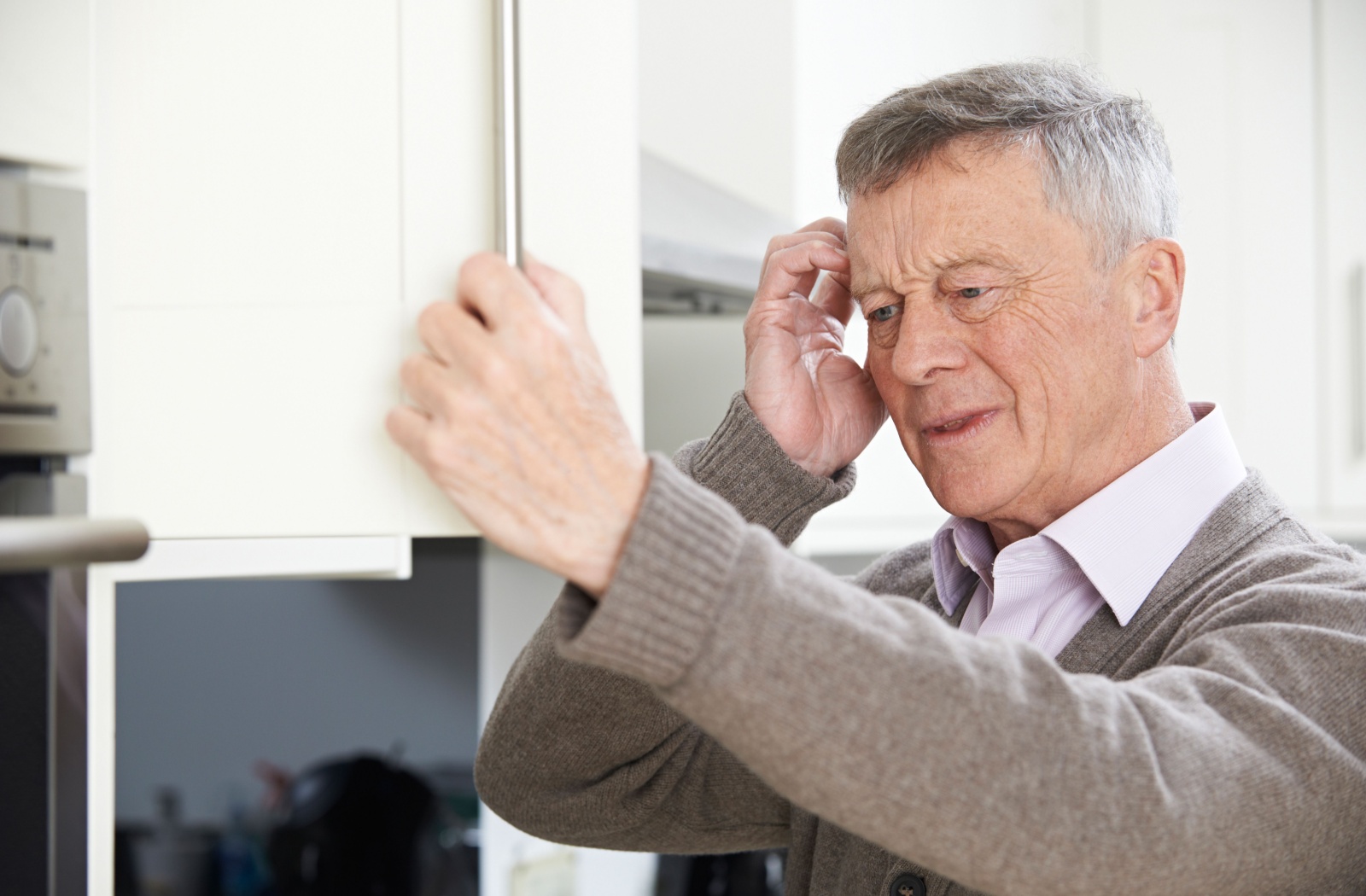 An older adult scratching in their head while looking in a cupboard in confusion due to age-related forgetfulness.