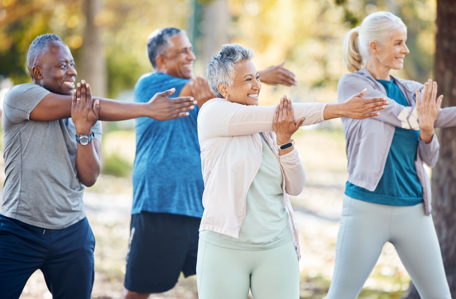 A group of older adults doing stretching and light exercise in the park together.