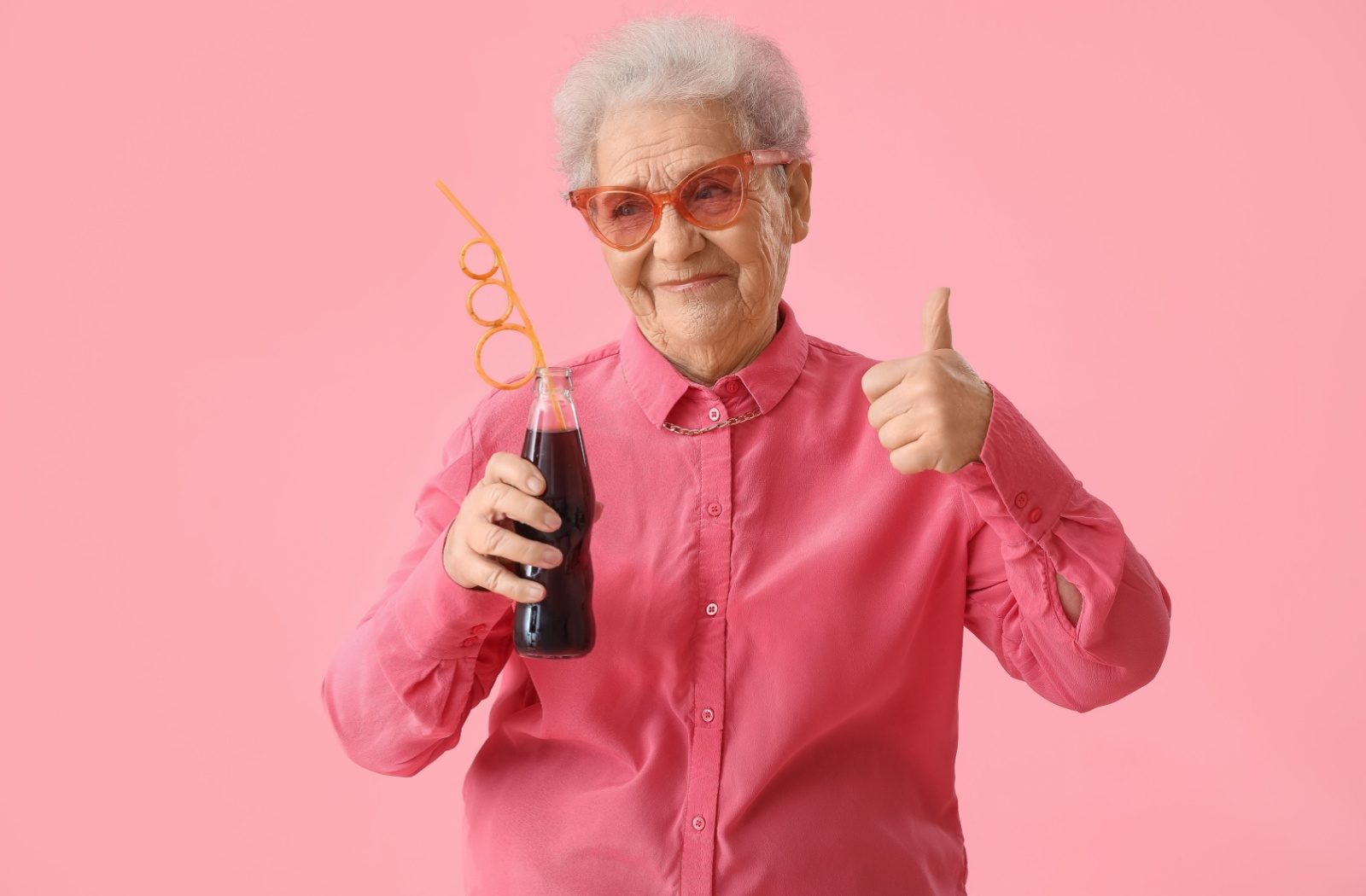 An older adult gives a thumbs up with one hand while holding a glass bottle of diet soda in the other.