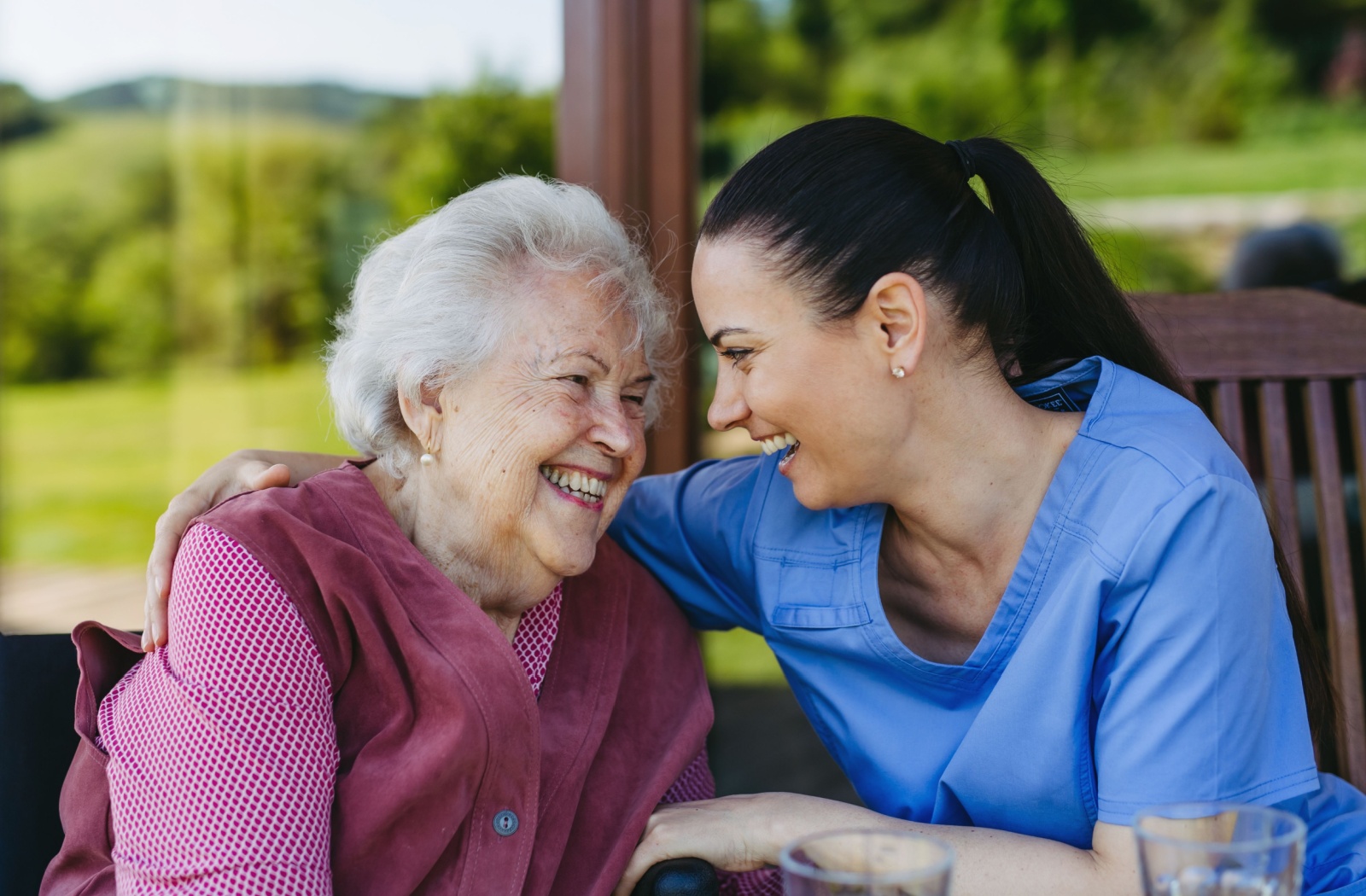 A caregiver and an older adult with dementia laughing together on a porch in memory care.