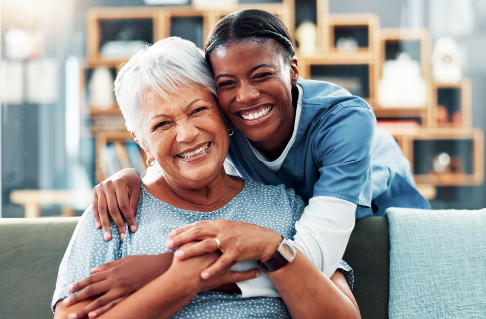 A caregiver in memory care hugs a grinning resident from behind

