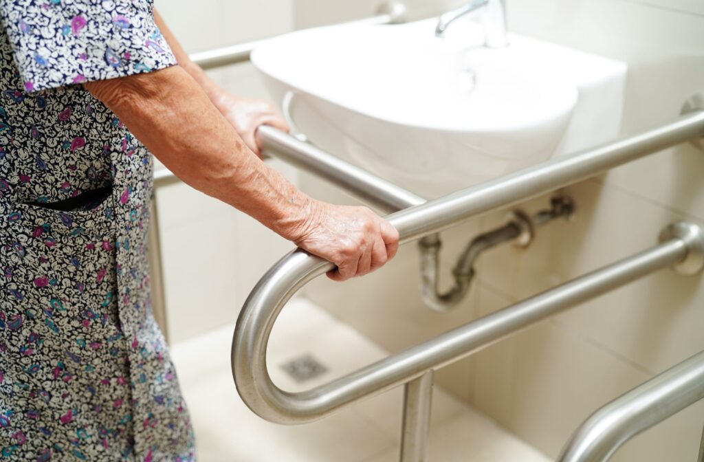 An older adult holds on to metal bars for support in the bathroom as they go to wash their hands.
